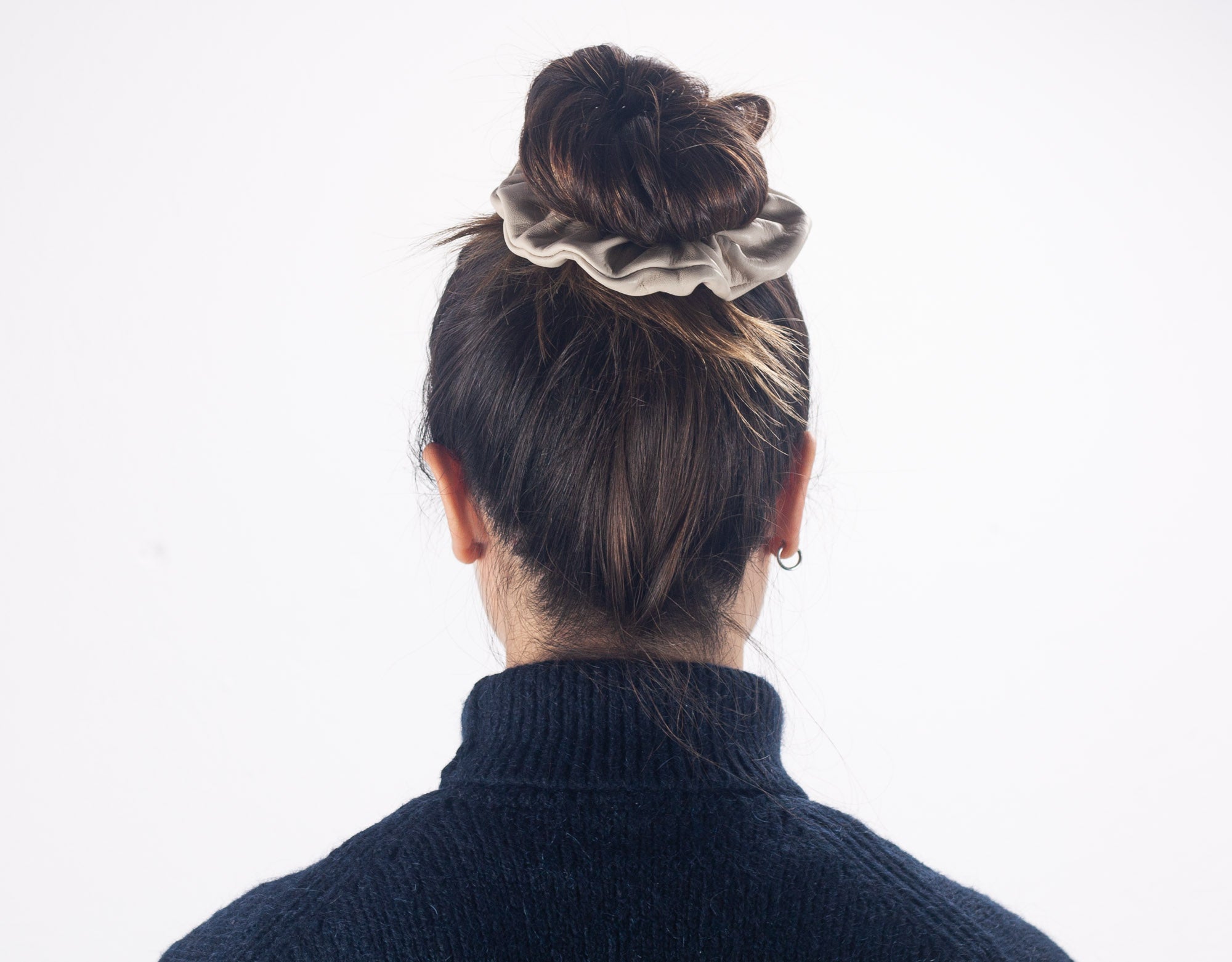 Person wearing a black turtleneck sweater with a scrunchie in their hair on a white background