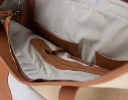 Close-up of the interior of a tote bag showing a light beige fabric lining, tan leather trim, and a zippered pocket.