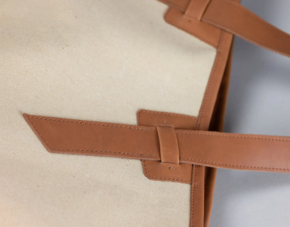 Close-up of a beige canvas tote bag with a tan leather strap and buckle detail.