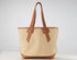 A canvas tote bag with a natural beige body and tan leather handles, trim, and base, photographed against a neutral light gray background.