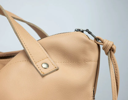 Beige leather handbag with a strap on a light gray background