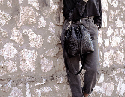 Person holding a textured black handbag against a stone wall