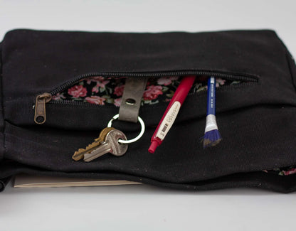 Black pouch with keys and pens peeking out on a light gray background