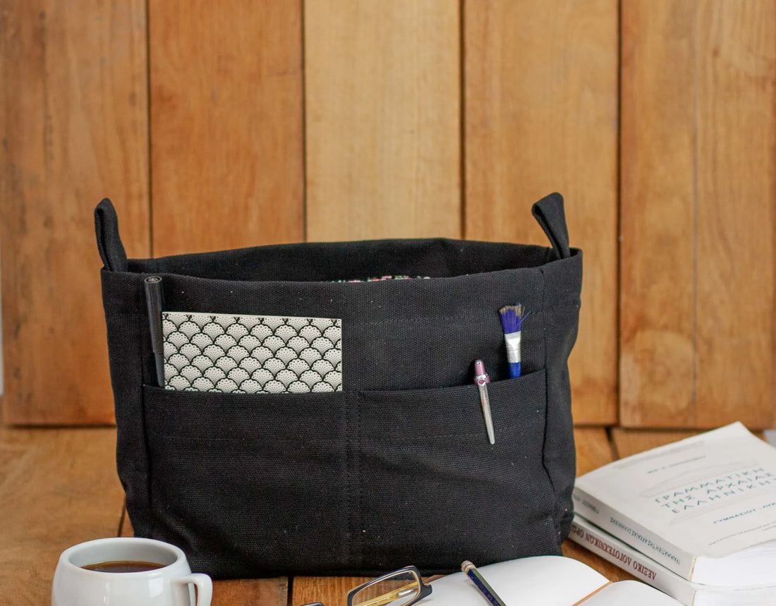 Black fabric basket with pockets on a wooden surface with stationery items.