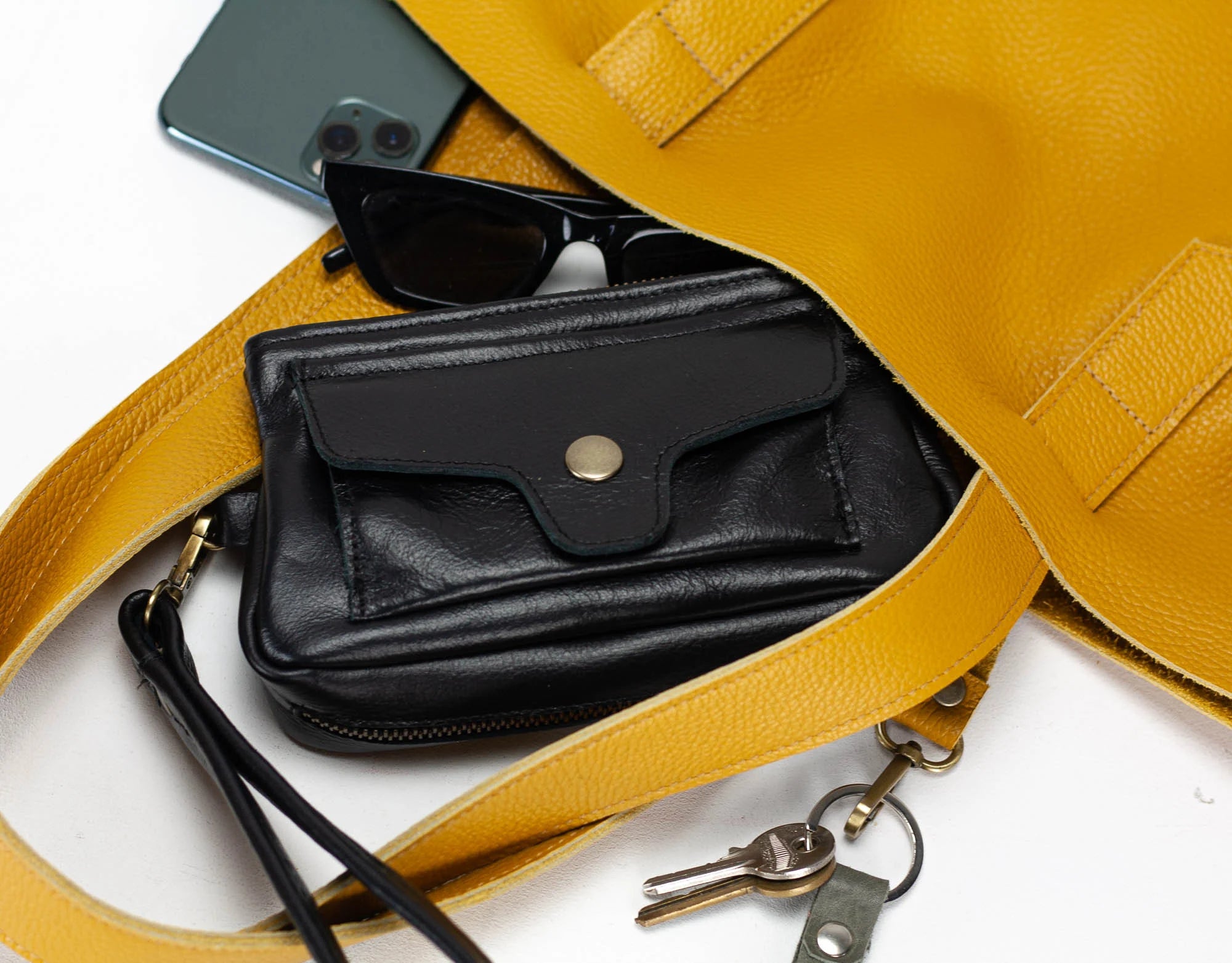 Yellow leather bag with black wallet, sunglasses, and keys on a white background