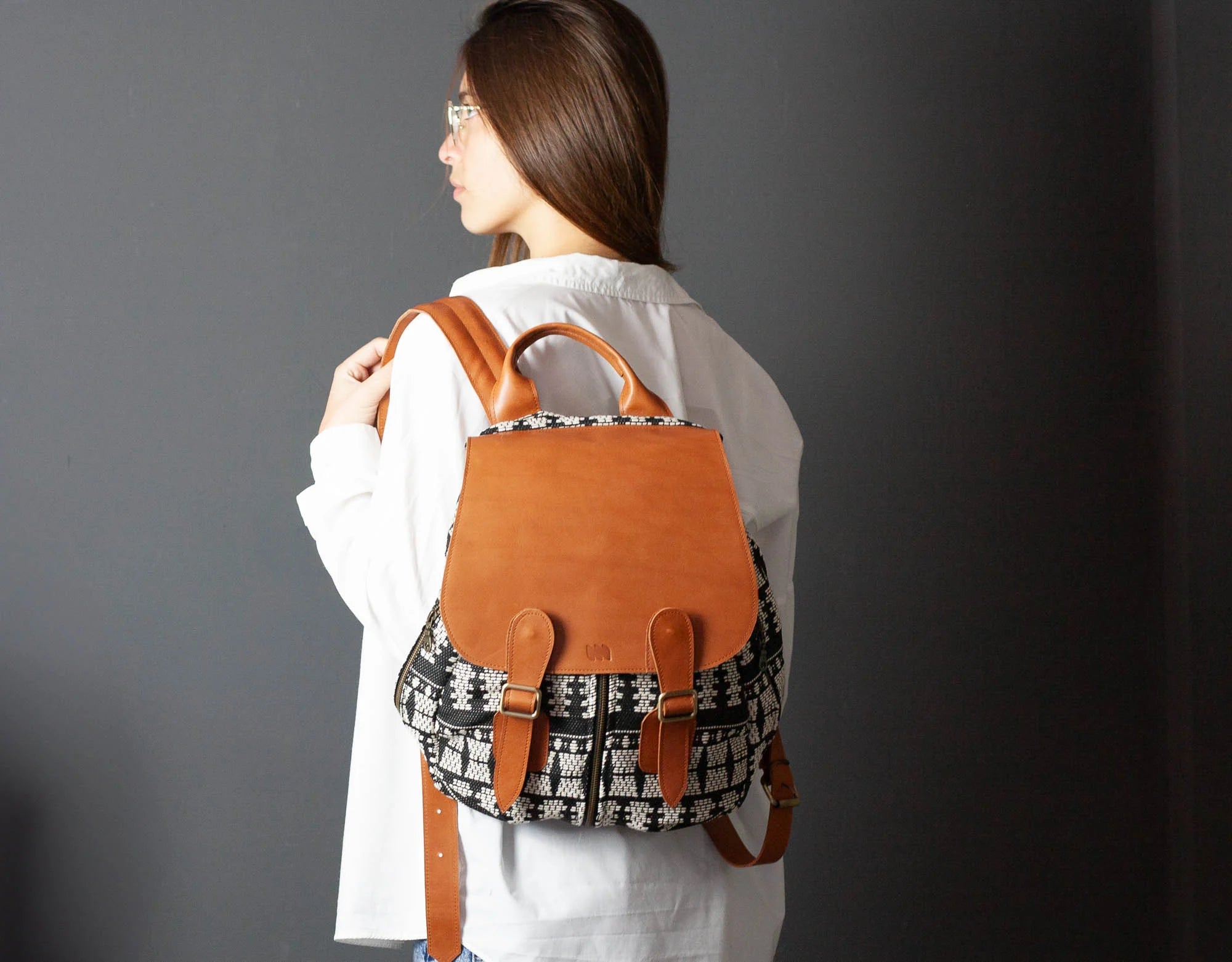 Person wearing a brown leather backpack with a plain background