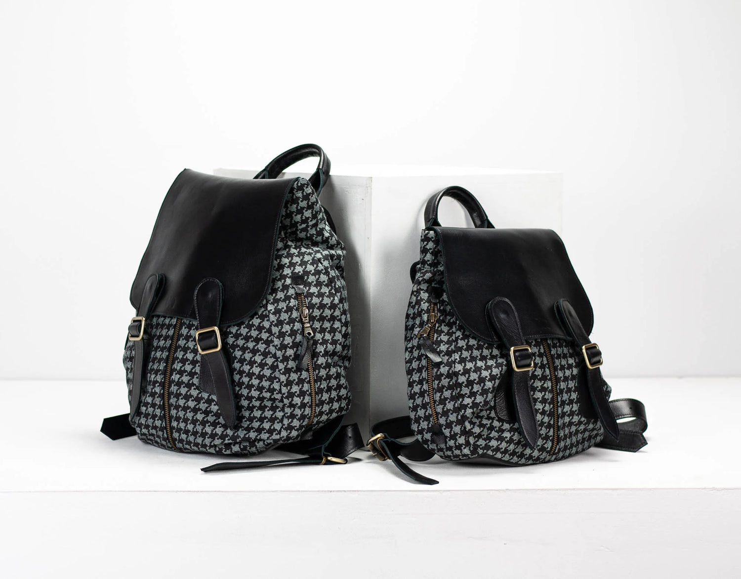 Two backpacks, one with a houndstooth pattern and the other black, on a white background.