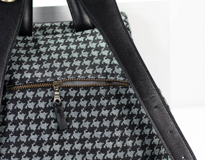 Close-up of a black and gray houndstooth patterned bag with a gold zipper on a white background.