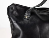 Close-up of a black leather handbag with a visible zipper on a light gray background