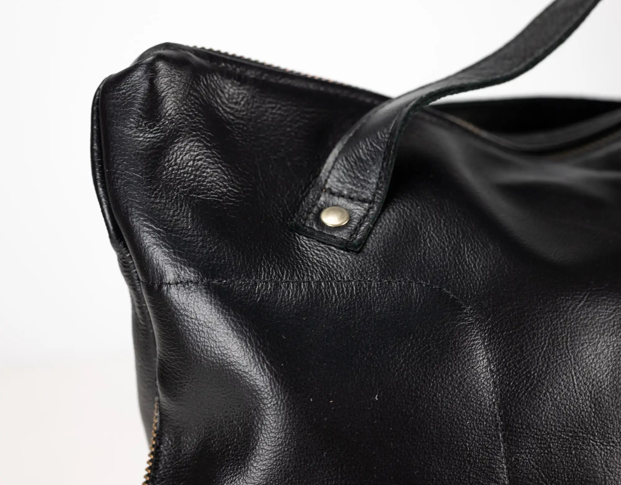 Close-up of a black leather handbag with a visible zipper on a light gray background