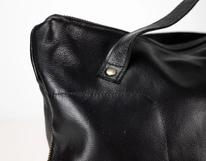 Close-up of a black leather handbag with a visible zipper on a light gray background