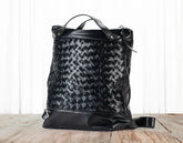Black woven leather bag on a wooden surface with a white background