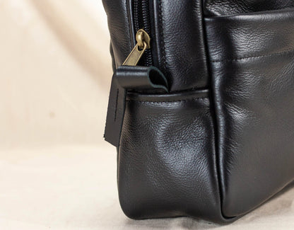 Close-up of a black leather bag with a gold zipper on a beige background