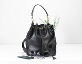 Black leather bucket bag with sunglasses and phone on a white background