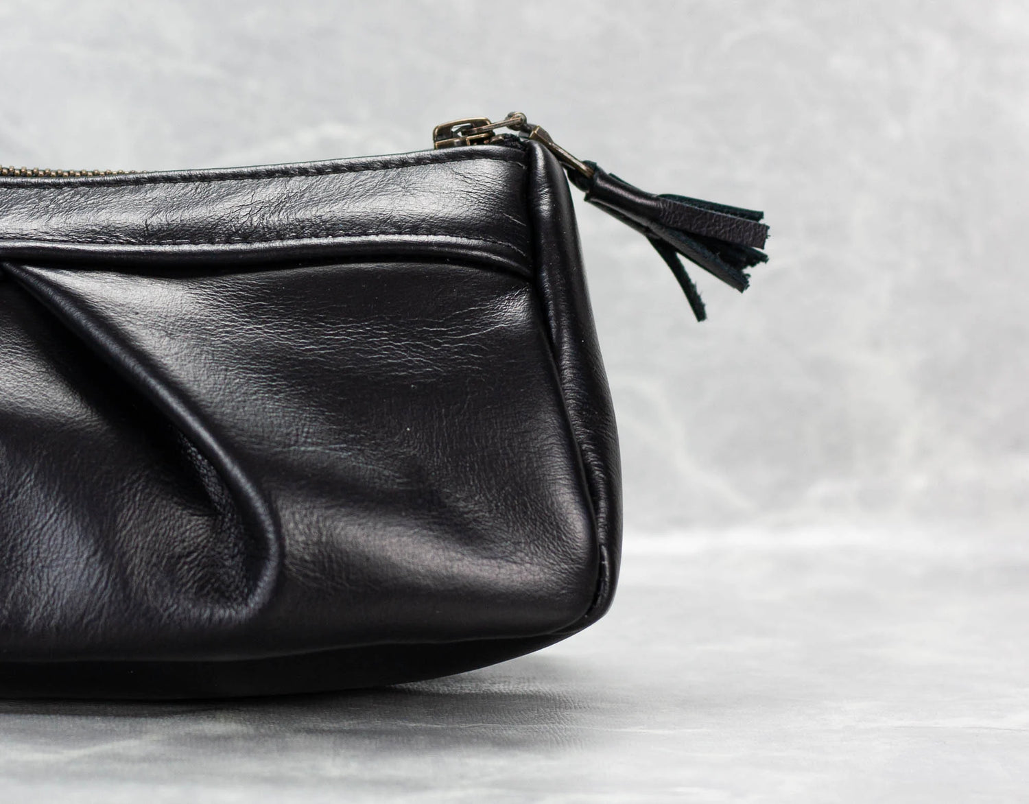 Black leather clutch bag with a tassel on a light gray background