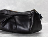 Black leather handbag with a zipper on a light gray background