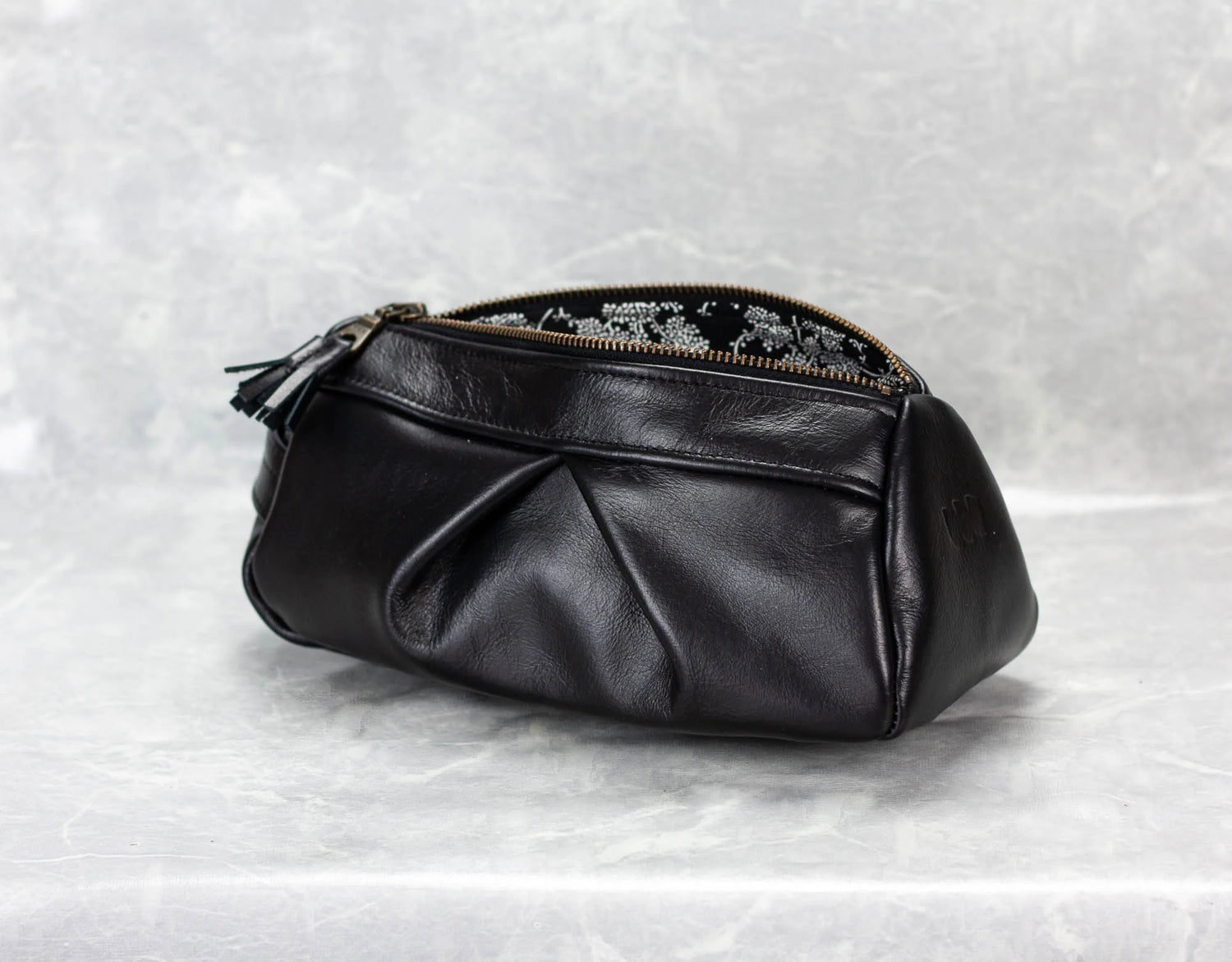 Black leather pouch with floral embroidery on a textured white background