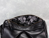 Black leather bag with floral embroidery on a textured gray background