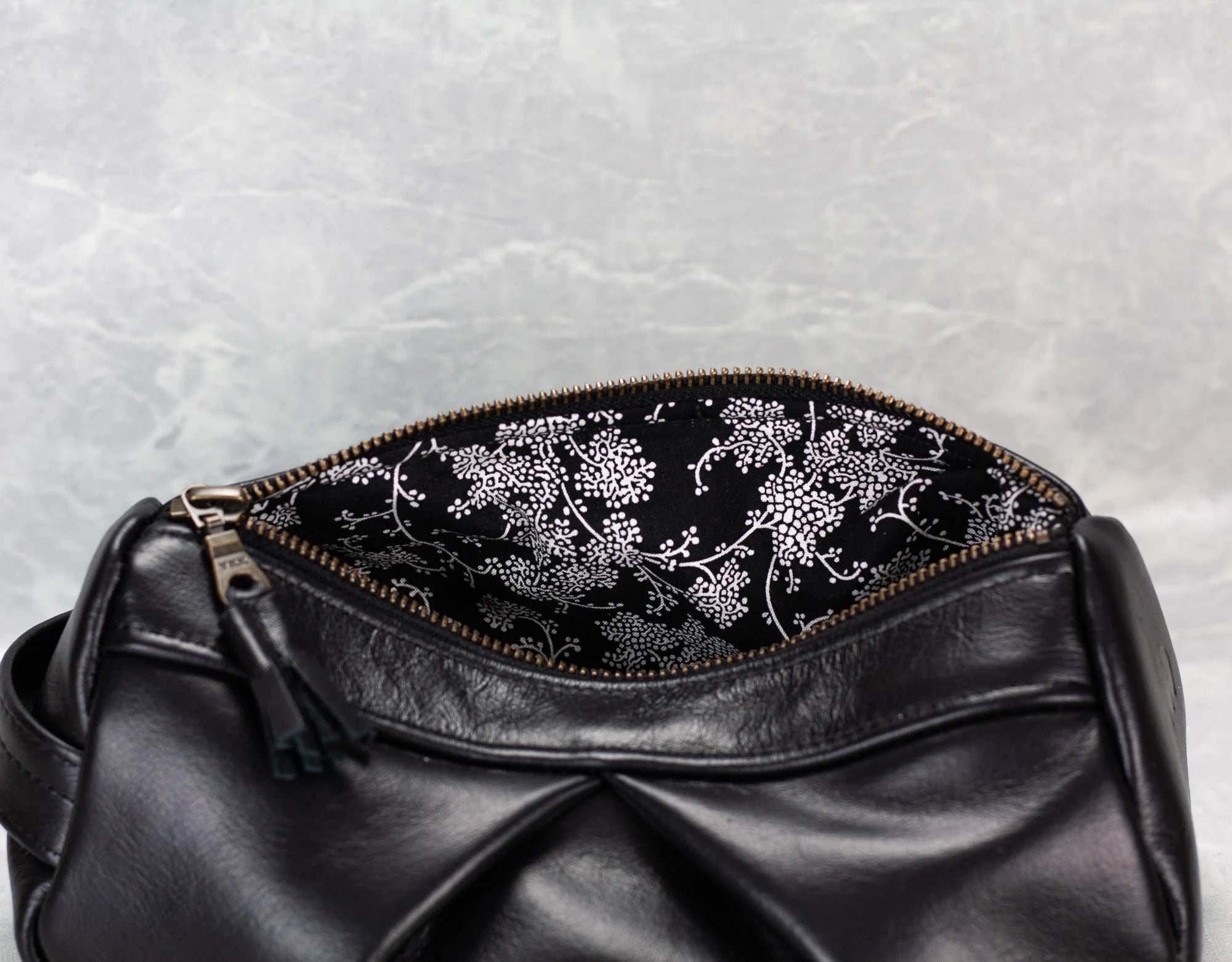 Black leather bag with floral embroidery on a textured gray background