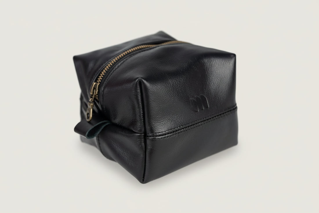 Black leather toiletry bag with gold zipper on a white background