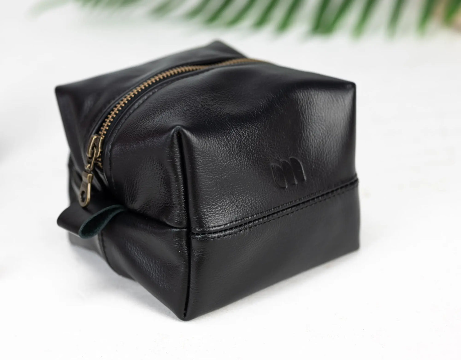 Black leather toiletry bag with gold zipper on a white background
