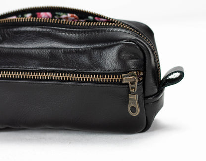 Black leather dopp kit with gold zipper on a white background