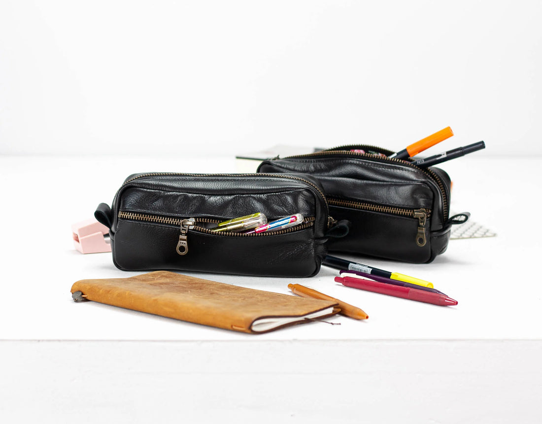 Black leather pencil cases with pens on a white background