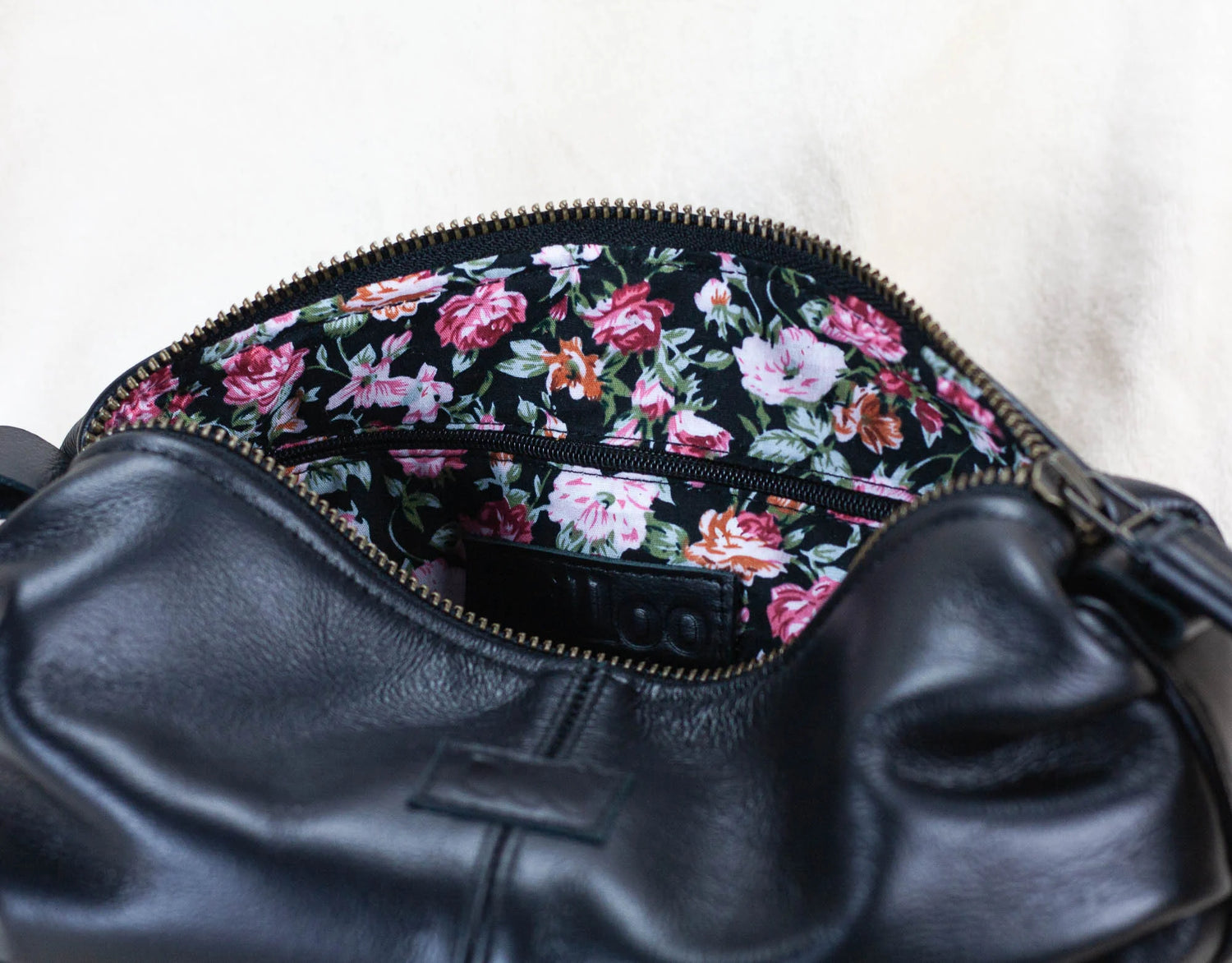 Black leather bag with floral patterned zipper on a white background