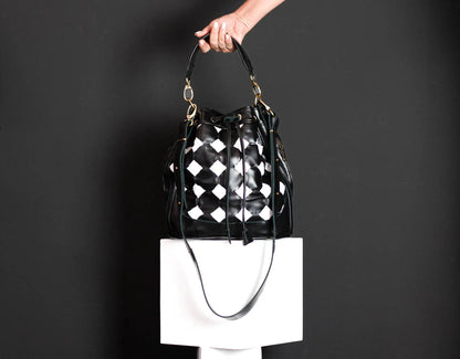 Black and white checkered handbag held by a person against a dark background