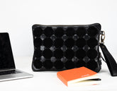 Black textured pouch next to a laptop and books on a white background