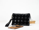 Black quilted clutch bag with a strap on a white background