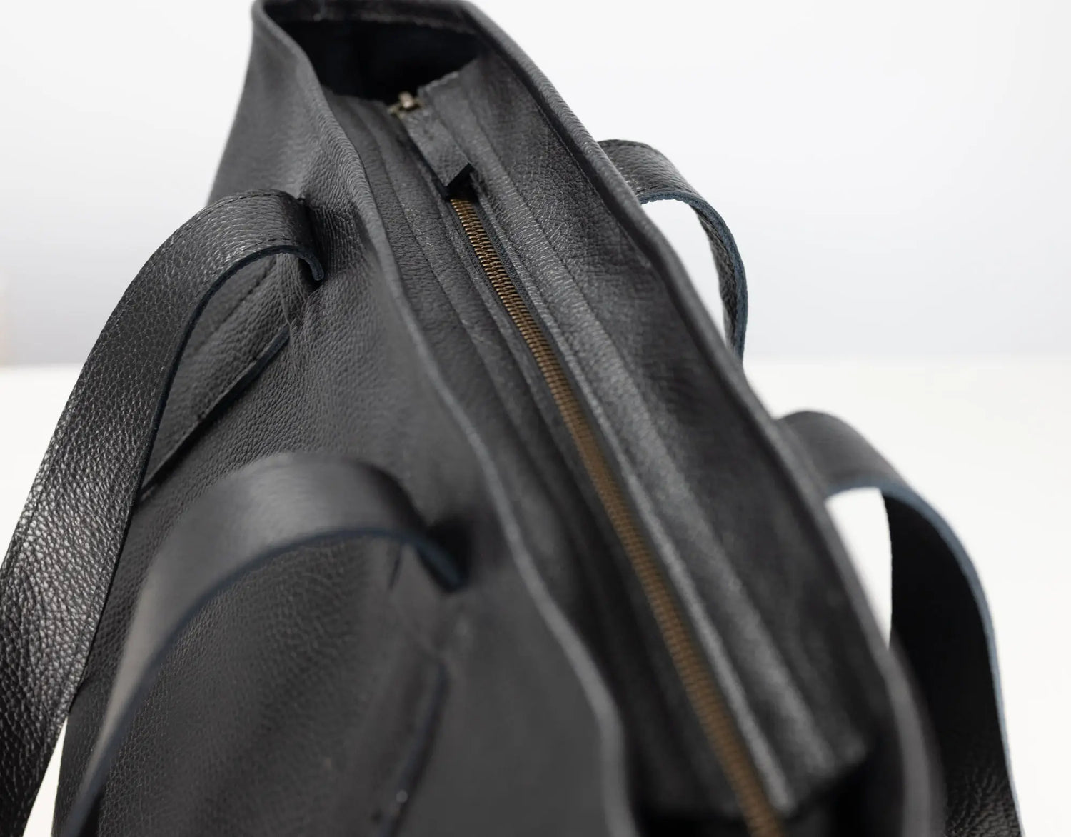 Close-up detail of a black leather tote bag showing the interior opening with a gold-toned zipper and part of the strap.