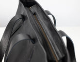 Close-up detail of a black leather tote bag showing the interior opening with a gold-toned zipper and part of the strap.