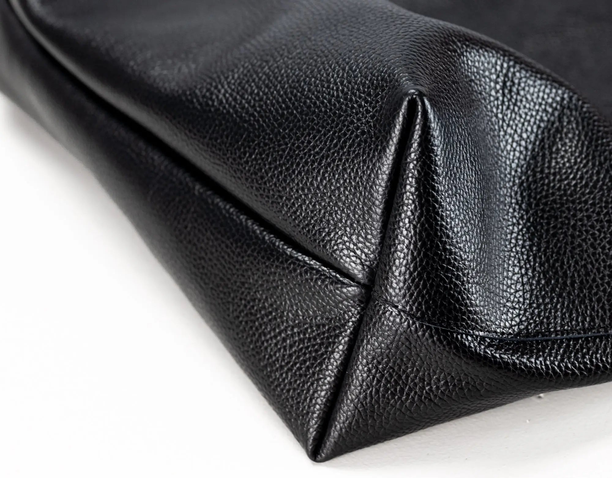 Close-up of a black pebbled leather clutch or pouch corner showing the texture and stitching on a white background.