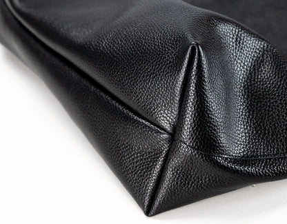 Close-up of a black pebbled leather clutch or pouch corner showing the texture and stitching on a white background.
