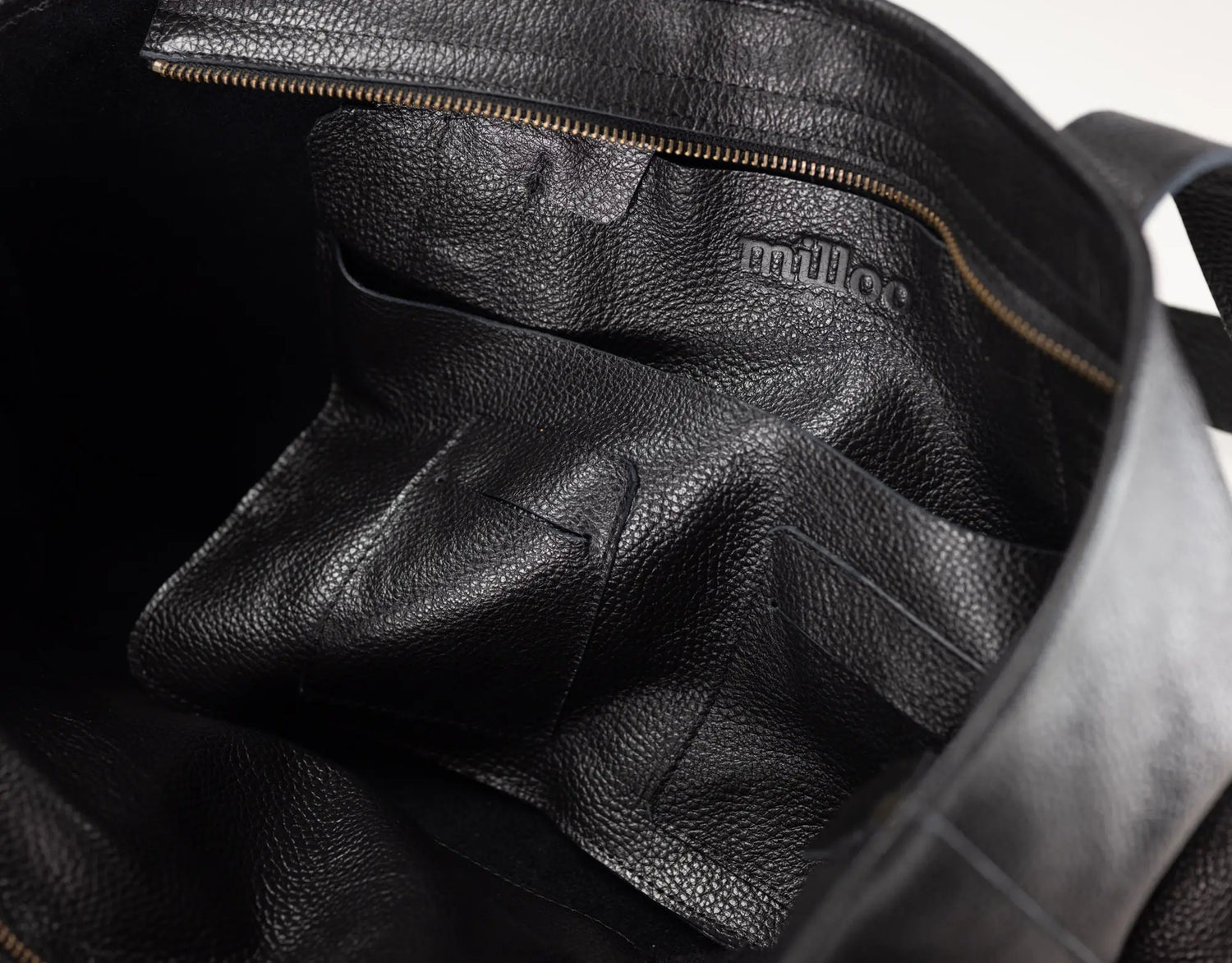 Close-up of the interior of a black pebbled leather bag, showing a zippered compartment and the embossed brand name &