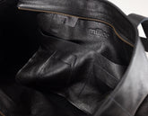 Close-up of the interior of a black pebbled leather bag, showing a zippered compartment and the embossed brand name &