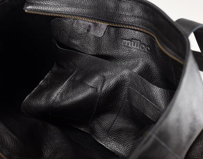 Close-up of the interior of a black pebbled leather bag, showing a zippered compartment and the embossed brand name &