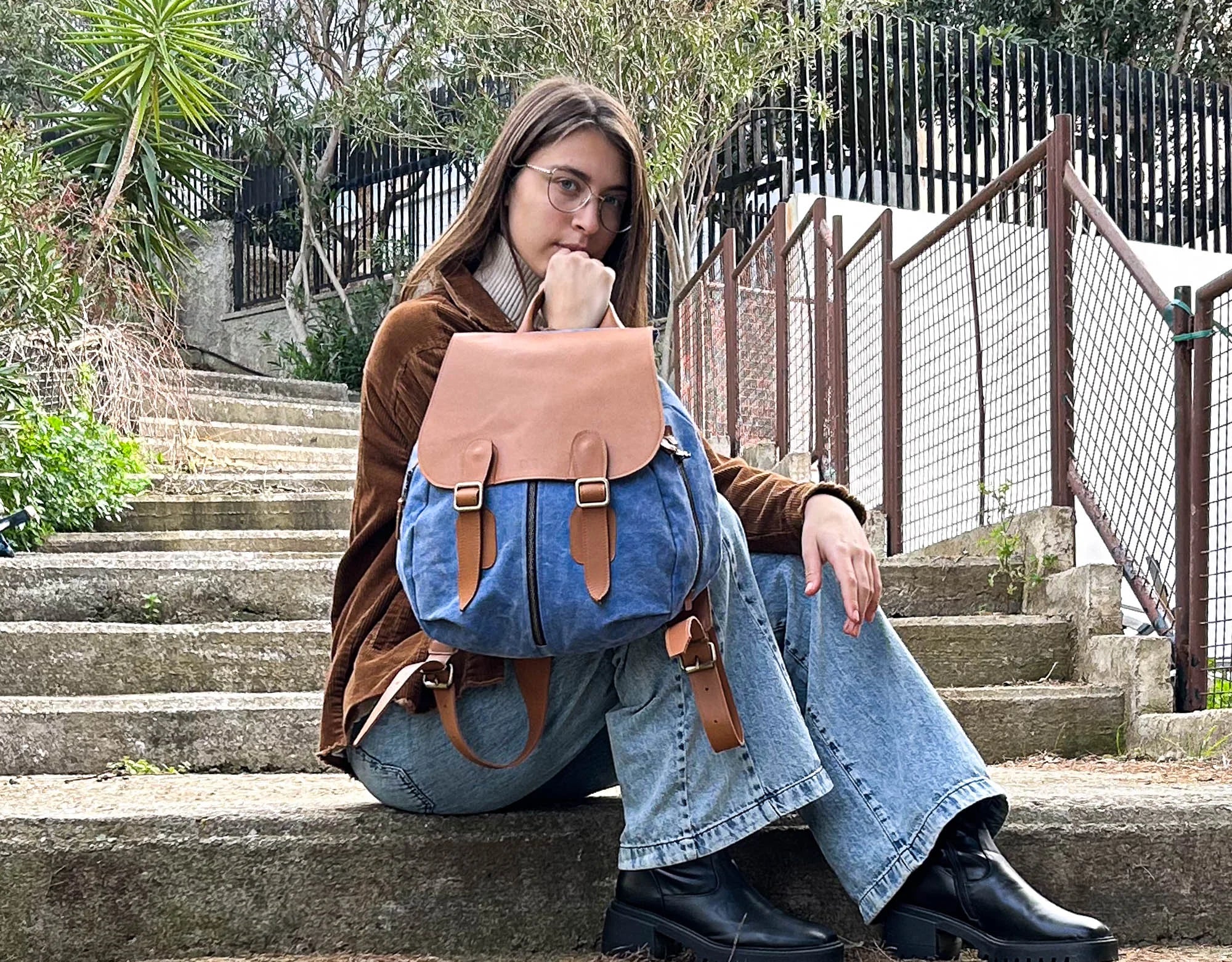 Person sitting on steps wearing a blue backpack with brown leather straps.