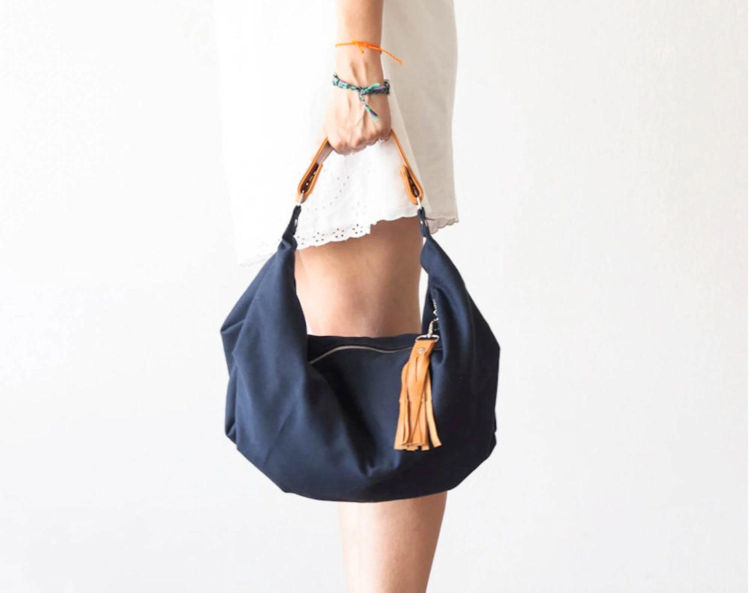 Navy blue handbag with a tassel held by a person on a white background