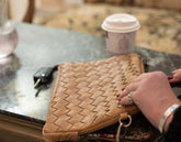 Brown woven clutch on a glass table with a coffee cup in the background