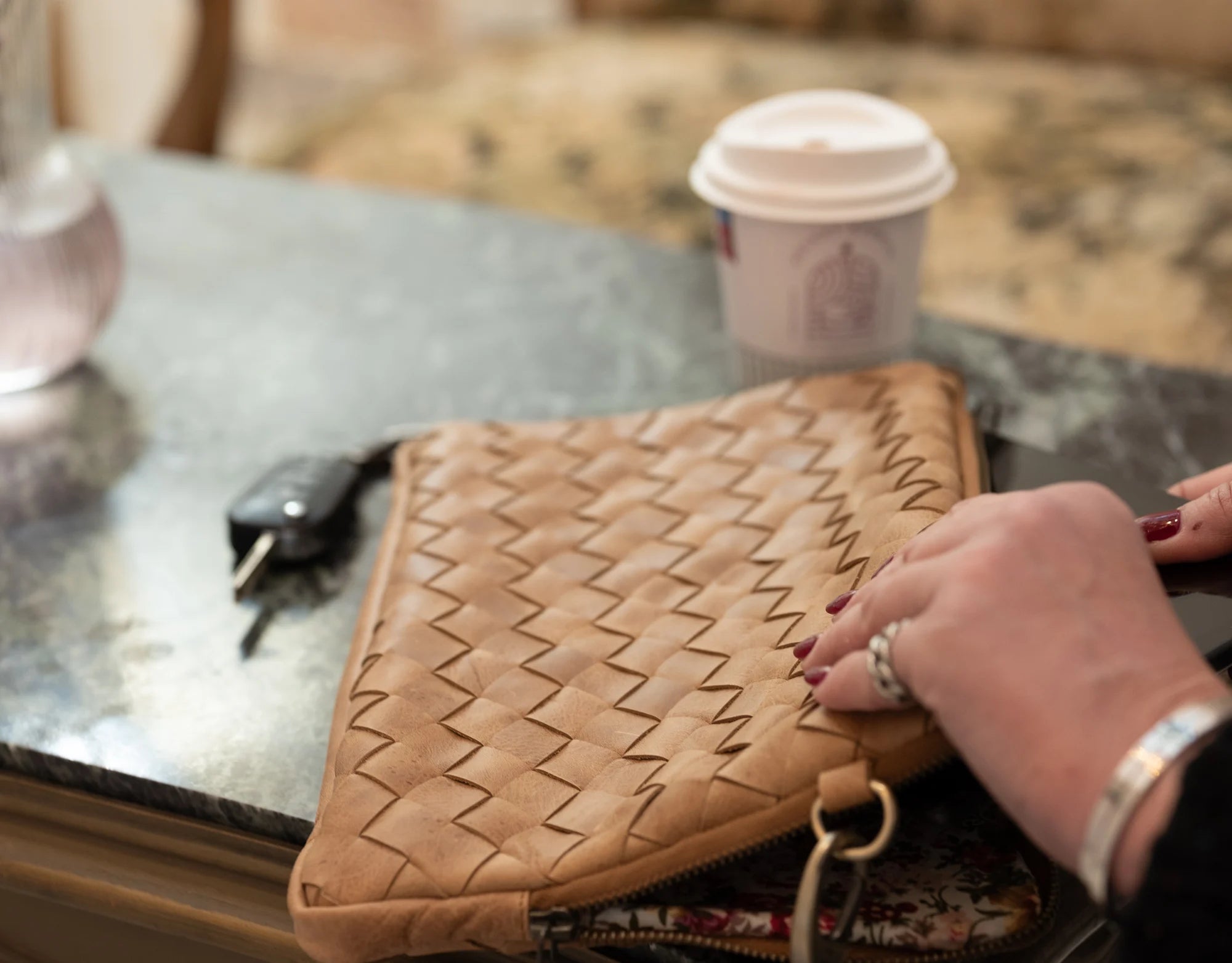 Brown woven clutch on a glass table with a coffee cup in the background
