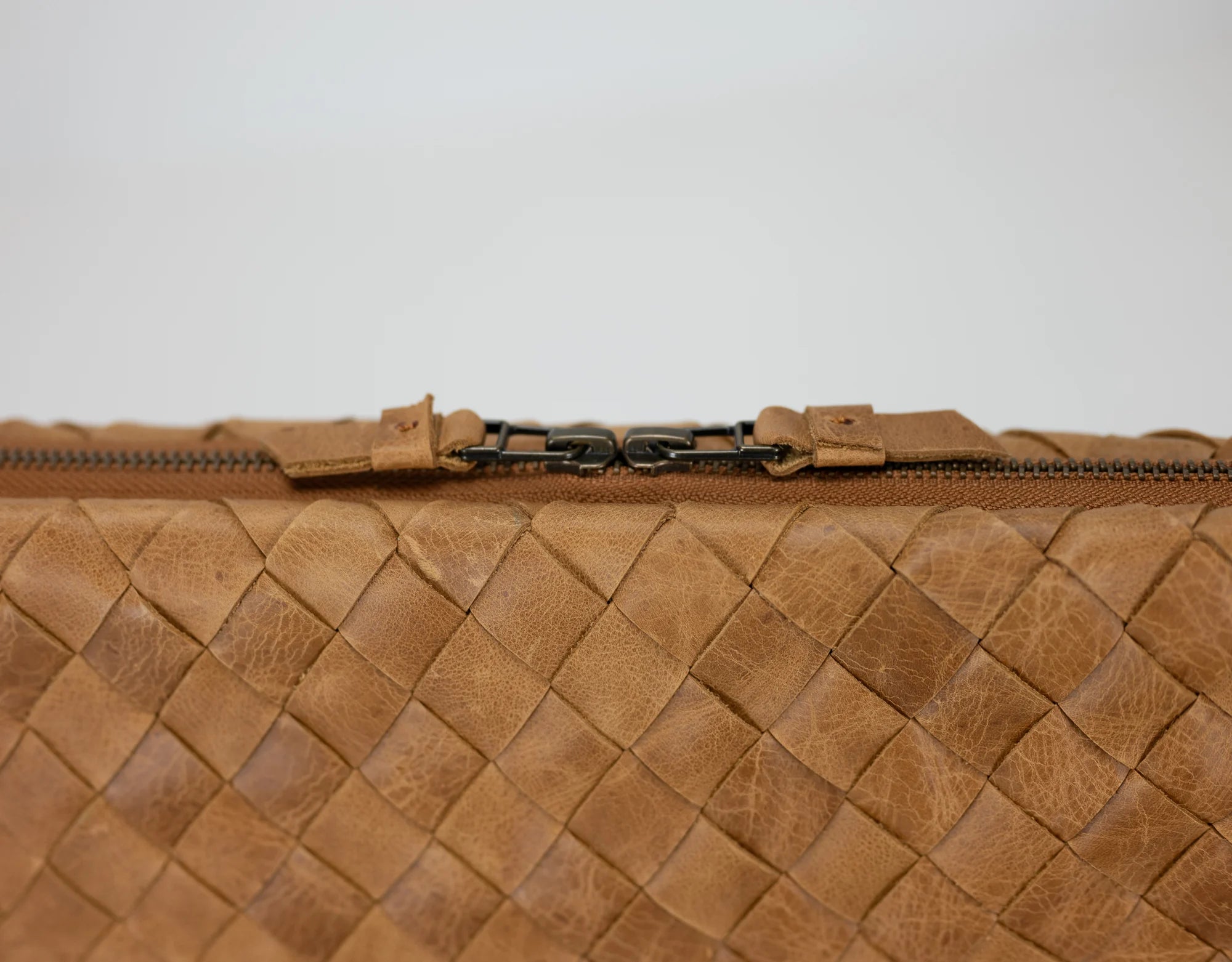 Close-up of a brown woven leather clutch bag with a zipper on a light gray background