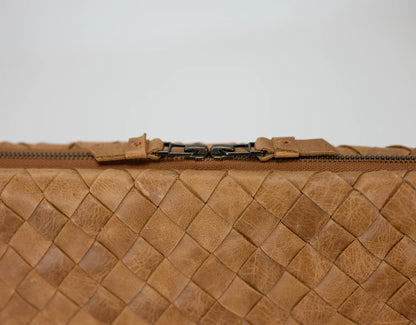 Close-up of a brown woven leather clutch bag with a zipper on a light gray background