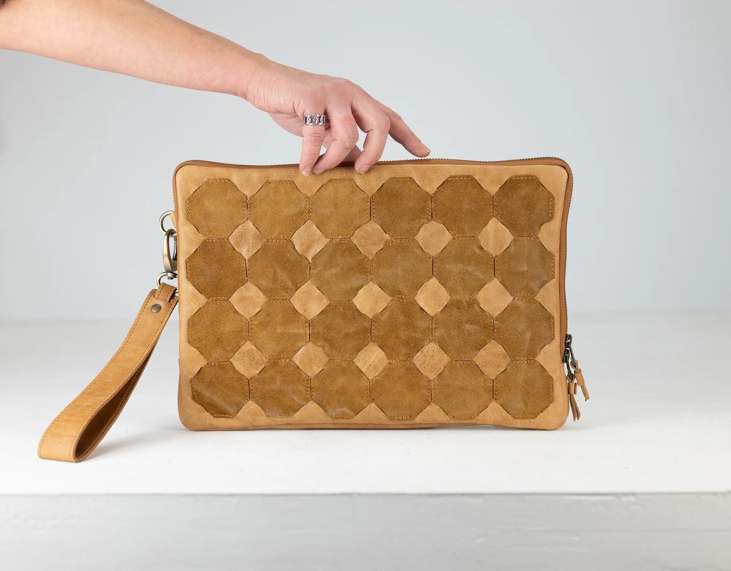 Brown textured clutch bag with a hand holding it against a light gray background