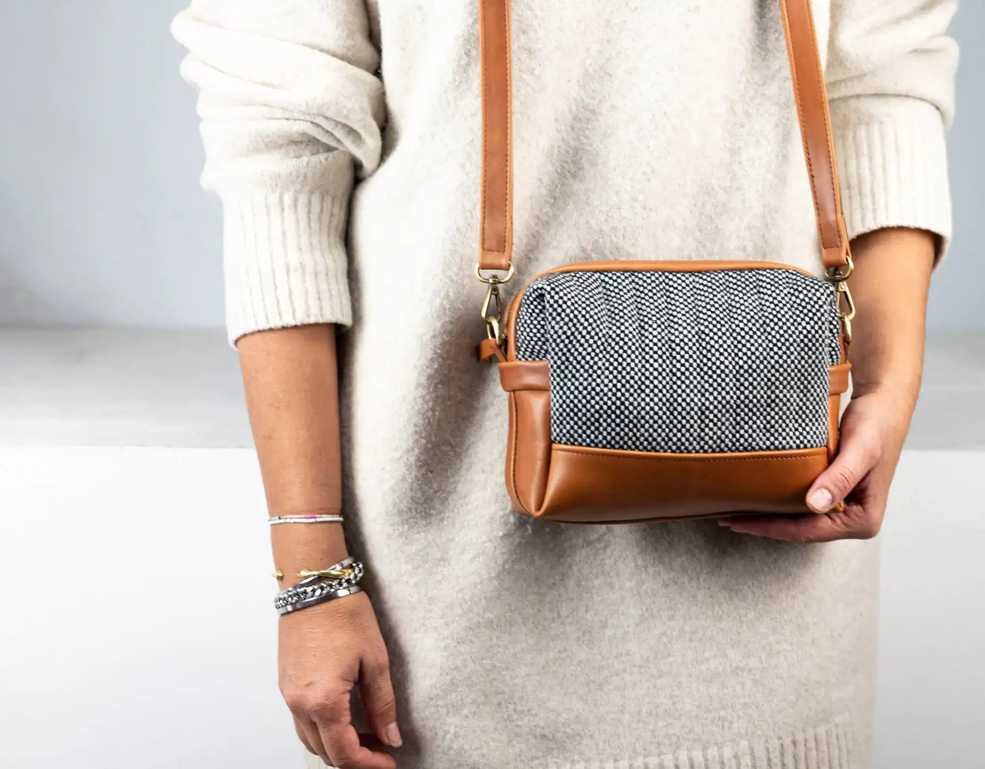 Person holding a crossbody bag with a textured pattern and brown leather accents.