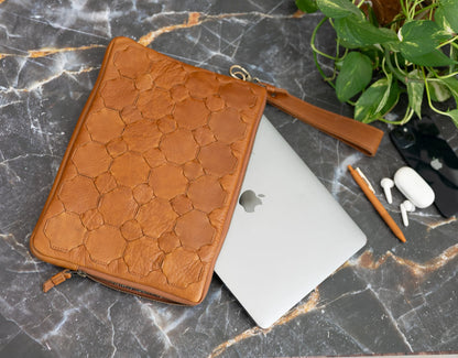 Brown leather case on a laptop with a marble surface and plant in the background