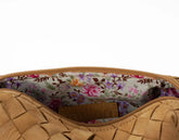 Close-up of a tan woven handbag with a floral interior lining.