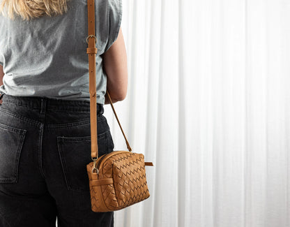 Person wearing a brown leather crossbody bag against a white curtain background