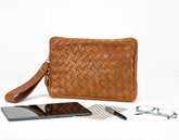 Brown woven clutch bag with phone, glasses, and pen on a white background